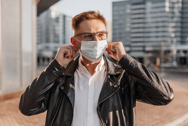 Handsome man putting on a medical protective mask on his face with glasses on a big city street on an urban background - Foto, Imagen