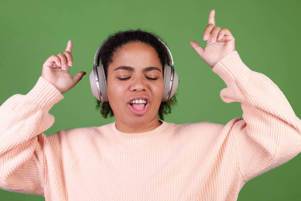 Beautiful african american woman on green background with wireless headphones listen music enjoying song  dancing moving positive - Zdjęcie, obraz
