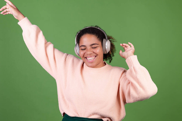 Beautiful african american woman on green background with wireless headphones listen music enjoying song  dancing moving positive - Foto, imagen
