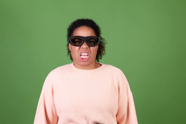 Krásná africká americká žena na zeleném pozadí s 3D kino brýle sledování film znechucení emoce - Fotografie, Obrázek