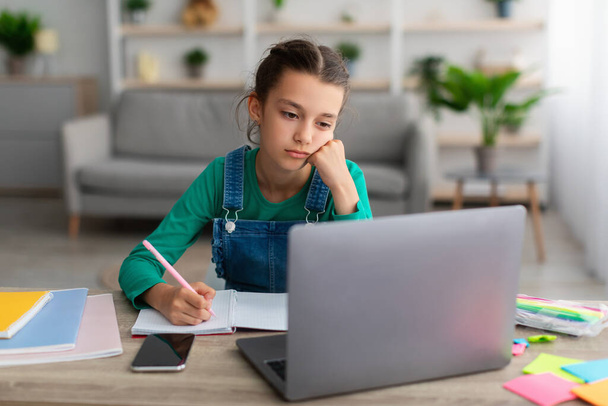 Втомлена шкільна дівчина пише в блокноті, роблячи домашнє завдання
 - Фото, зображення