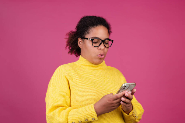Beautiful african american woman on pink background typing message on mobile phone focused thoughtful - Zdjęcie, obraz