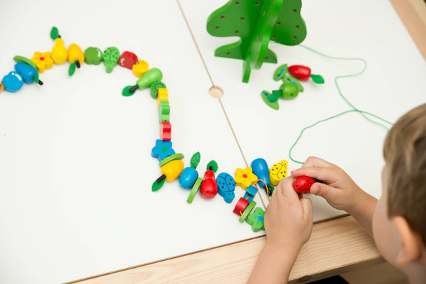 Feinmotorische Fähigkeiten. Stringing Beads Spielzeug für Säuglinge und Kleinkinder. Fadenaktivität für Kinder. Junge sitzt auf dem Boden und spielt mit Holzbaum und Gartenutensilien. - Foto, Bild