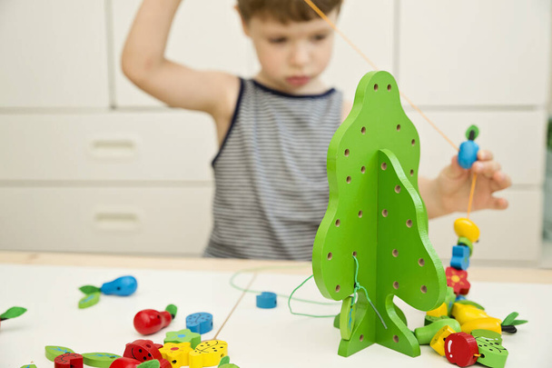 Feinmotorische Fähigkeiten. Stringing Beads Spielzeug für Säuglinge und Kleinkinder. Fadenaktivität für Kinder. Junge sitzt auf dem Boden und spielt mit Holzbaum und Gartenutensilien. - Foto, Bild