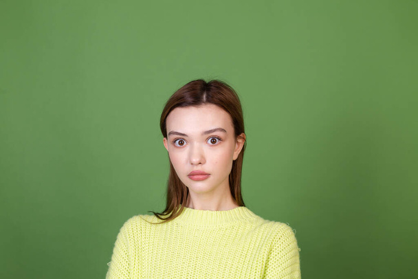 Молодая женщина с чистой идеальной натуральной кожей и макияжем коричневые большие губы на зеленом фоне шокированы глазами, открытыми широкий взгляд на камеру - Фото, изображение