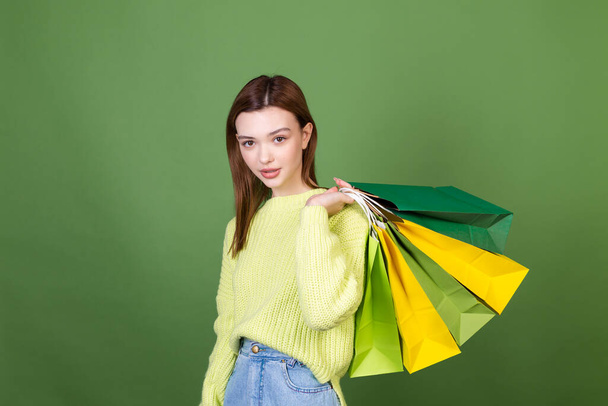Young woman with perfect  natural makeup brown big lips on green background holds shopping bags happy excited - Фото, зображення