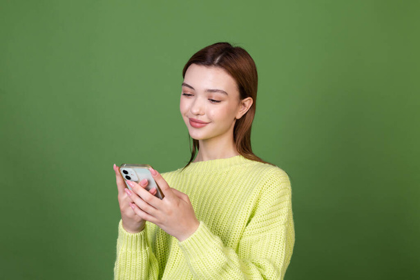 Молода жінка з ідеальним натуральним макіяжем коричневі великі губи на зеленому тлі дивиться на мобільний телефон мило впевнена посмішка
 - Фото, зображення