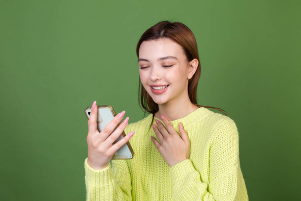 Mujer joven con maquillaje natural perfecto grandes labios marrones sobre fondo verde mirada en el teléfono móvil linda sonrisa risa - Foto, Imagen