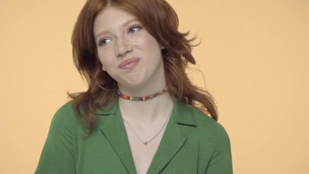 pozytywna nastolatka dziewczyna dostosowując czerwone włosy izolowane na żółte - Materiał filmowy, wideo