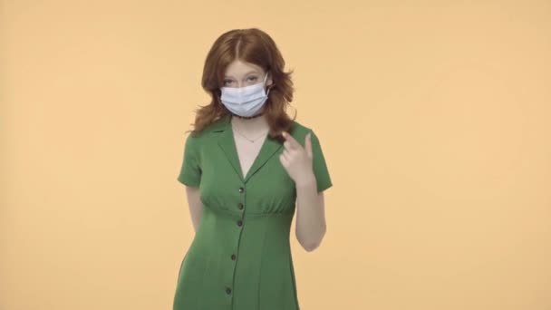 rousse adolescent fille pointant vers masque médical isolé sur jaune - Séquence, vidéo