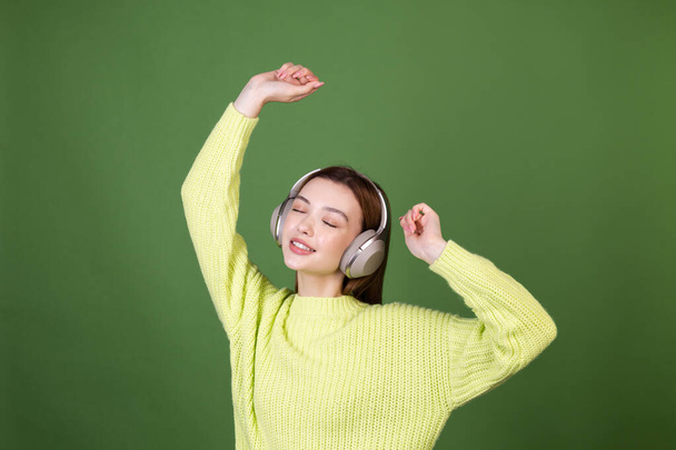 若いです女性とともに完璧なナチュラルメイク茶色大きな唇でカジュアルセーターで緑の背景に無線ヘッドフォン幸せなダンス周りに移動 - 写真・画像