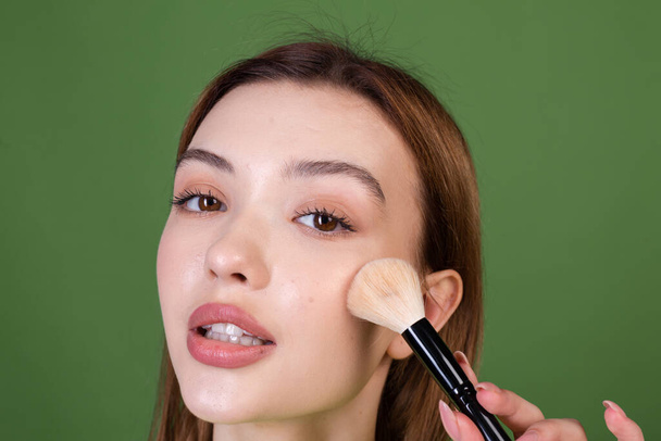 Young woman with perfect natural makeup brown big lips in casual sweater on green background holding blush brush posing - Φωτογραφία, εικόνα
