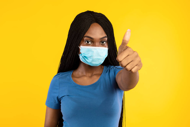Black Woman Wearing Face Mask Gesturing Thumbs-Up Over Yellow Background - Photo, Image