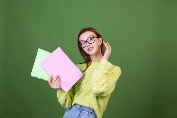 Молодая женщина с идеальным естественным макияжем коричневые большие губы в случайном свитере на зеленом фоне студент в очках и блокнотах счастливо улыбается позитивно - Фото, изображение
