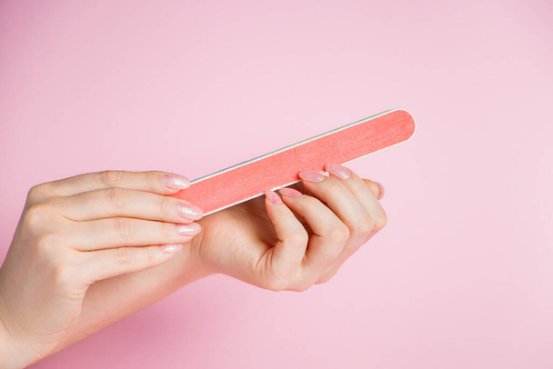 Woman does a manicure at home. Hands with a nail file on a pink background. - Foto, Imagen