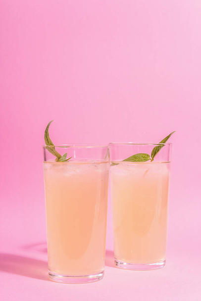 Summer refreshing cocktail. Cold sweet drink, modern hard light, dark shadow. Pastel pink background - Photo, image