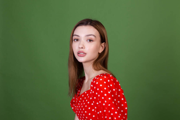 Jonge vrouw met perfecte natuurlijke make-up bruine grote lippen in polka stip rode jurk op groene achtergrond poseren - Foto, afbeelding