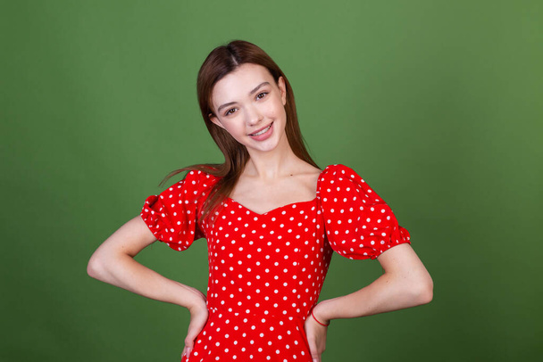 Jonge vrouw met perfecte natuurlijke make-up bruine grote lippen in polka stip rode jurk op groene achtergrond schattig glimlachen positief - Foto, afbeelding