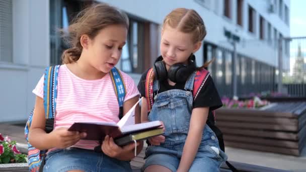  Zwei süße kaukasische Mädchen mit Rucksack sitzen und lesen Buch - Filmmaterial, Video