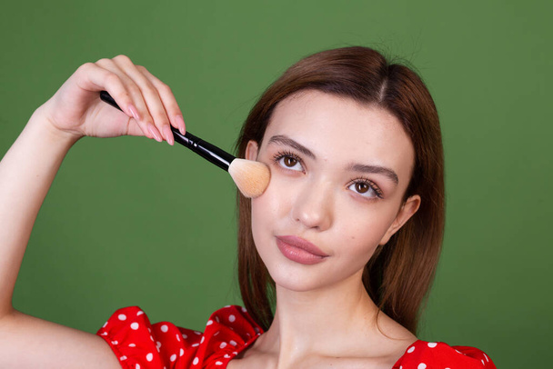 Young woman with perfect natural makeup brown big lips in polka dot red dress on green background holds blush brush fashion beauty portrait - Photo, Image