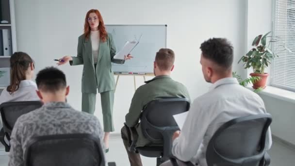 coach session, young woman manager presents a plan for a new project to employees on flipchart, man raises his hand and asks question during presentation in office - Footage, Video