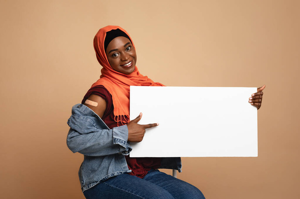Vrolijke Afrikaanse amerikaanse moslim vrouw werd gevaccineerd, met lege plakkaat - Foto, afbeelding