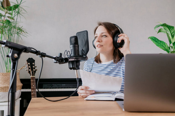 the stylish and educated caucasian woman records podcasts in a recording studio or in her home. the European millennial woman creates audio content or records text, records an audio book or radio show - Foto, afbeelding