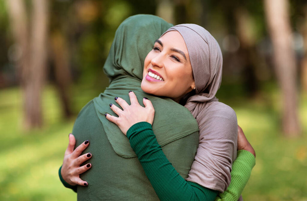 Due signore islamiche multirazziali che si abbracciano in piedi all'aperto - Foto, immagini