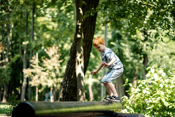 A young boy walks on a log at the playground. Active summer vacation. - Photo, image
