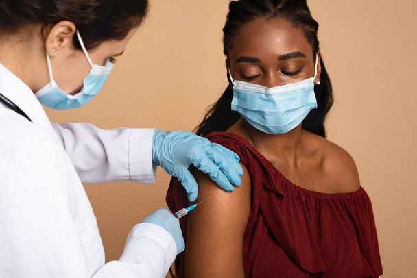 Pielęgniarka w odzieży roboczej szczepienia dla czarnej pani - Zdjęcie, obraz
