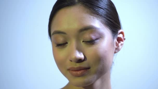 bonita mujer asiática con perfecta piel mirando a la cámara en azul - Imágenes, Vídeo