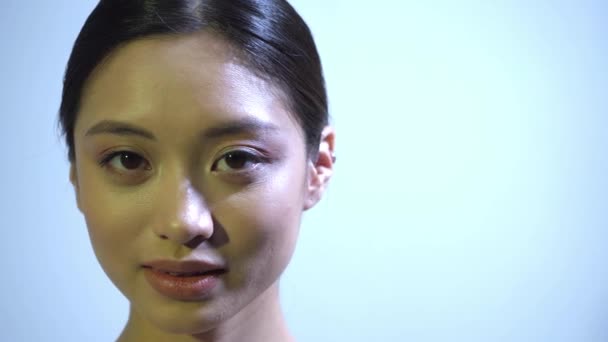 Mükemmel ciltli genç Asyalı kadın mavi kameraya bakıyor. - Video, Çekim
