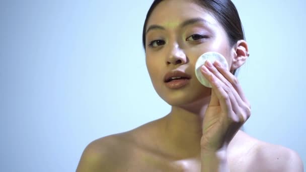 junge asiatische Frau reinigt Gesicht mit Wattepad auf blau - Filmmaterial, Video