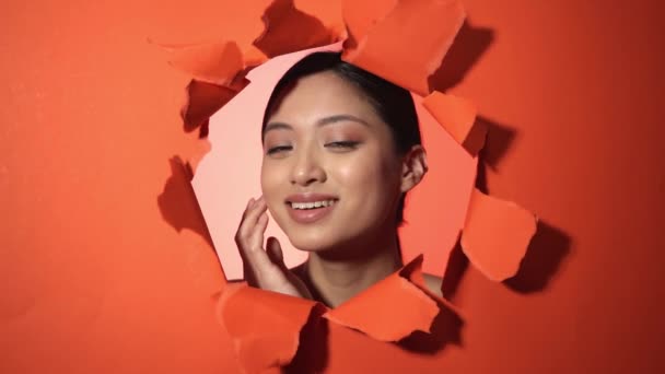 smiling asian woman touching skin near ripped paper orange background - Footage, Video