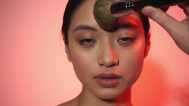 jonge aziatische vrouw aanbrengen gezicht poeder op roze - Video