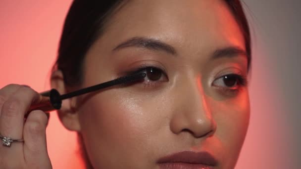 giovane donna asiatica che applica mascara sul rosa - Filmati, video