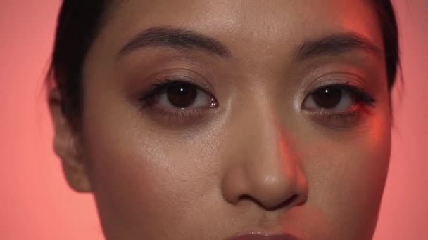 ピンクに隔離された肌に触れるアジア系の若い女性のクローズアップ - 映像、動画