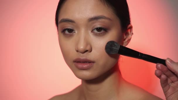 maquillaje artista aplicando cara en polvo en joven asiático mujer en rosa - Metraje, vídeo