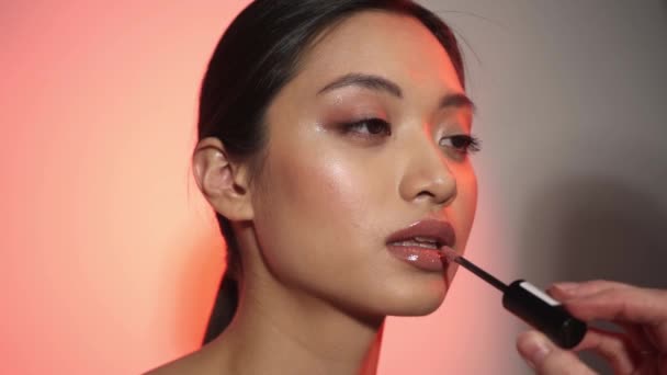 makeup artist εφαρμογή lip gloss σε νεαρή ασιατική γυναίκα σε ροζ και γκρι - Πλάνα, βίντεο
