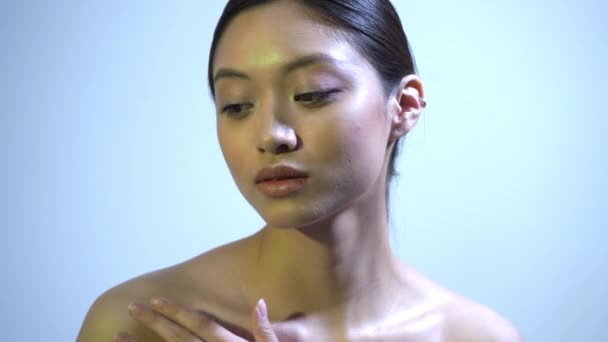 joven asiático mujer con desnudo hombros tocar clavícula en azul - Imágenes, Vídeo