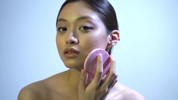 asiática mulher esfoliante pele no rosto com pedra-pomes no azul - Filmagem, Vídeo
