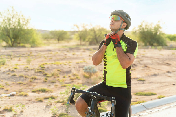 Önce güvenlik. Yolda bisiklet sürmeye başlamak için kask ve güneş gözlüğü takan Latin bir genç. Formda bisikletçi bisiklete binmeye hazırlanıyor - Fotoğraf, Görsel