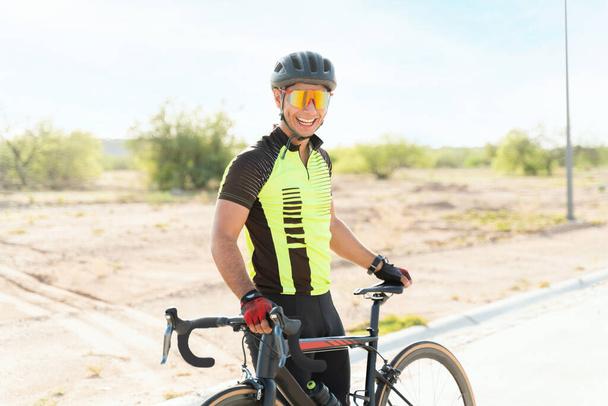 Ciclista profissional animado rindo e fazendo contato visual enquanto descansa de pedalar em uma estrada aberta - Foto, Imagem