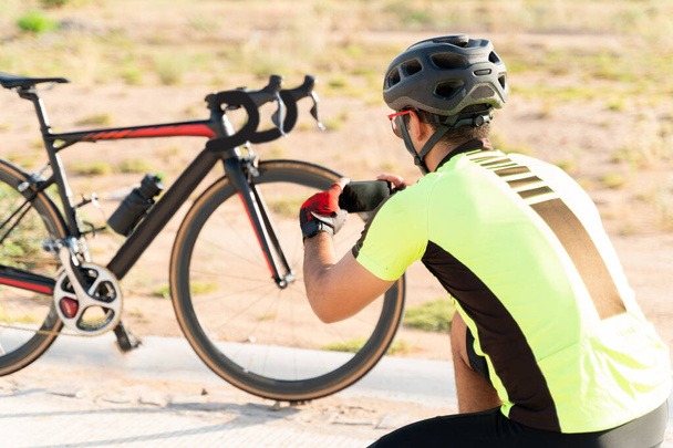 Ciclista latino tomando una foto con un smartphone de una bicicleta negra mientras se detiene en una carretera abierta para publicarla en las redes sociales  - Foto, Imagen