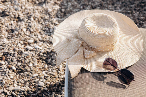 Women's straw hat with a bow and sunglasses on background of a pebble beach with shadow. Summer holiday, vacation and travel concept. Copy space - Foto, immagini