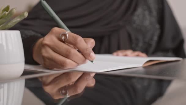 Piano primo piano di mani di donna musulmana irriconoscibile in abiti neri tradizionali prendere appunti in copybook mentre si lavora da casa - Filmati, video