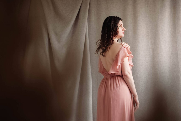 Beautiful brunette woman in a pink dress on a background of linen fabric. Copy, empty space for text. - Photo, Image