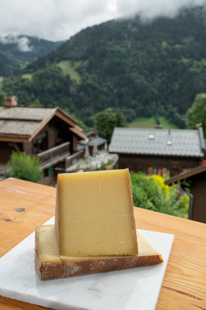 Sbírka sýrů, francouzský sýr comte, beaufort, abondance a francouzská horská vesnice v létě v Haute-Savoie na pozadí - Fotografie, Obrázek