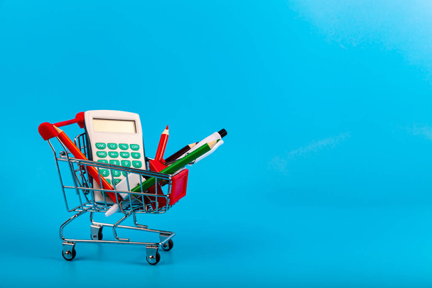 Stationery and shopping cart on a blue background. Shopping for school. Back to school. - Фото, изображение