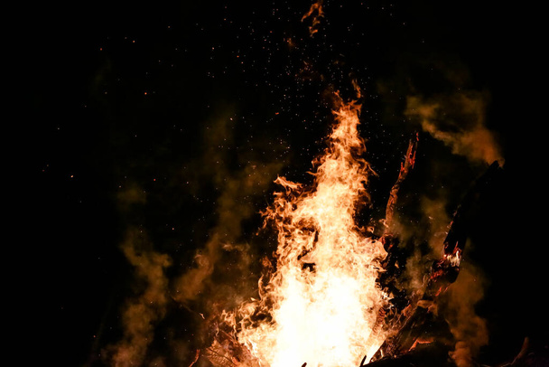 Огонь с дровами на земле красный огонь с черным фоном с красивыми искрами. - Фото, изображение